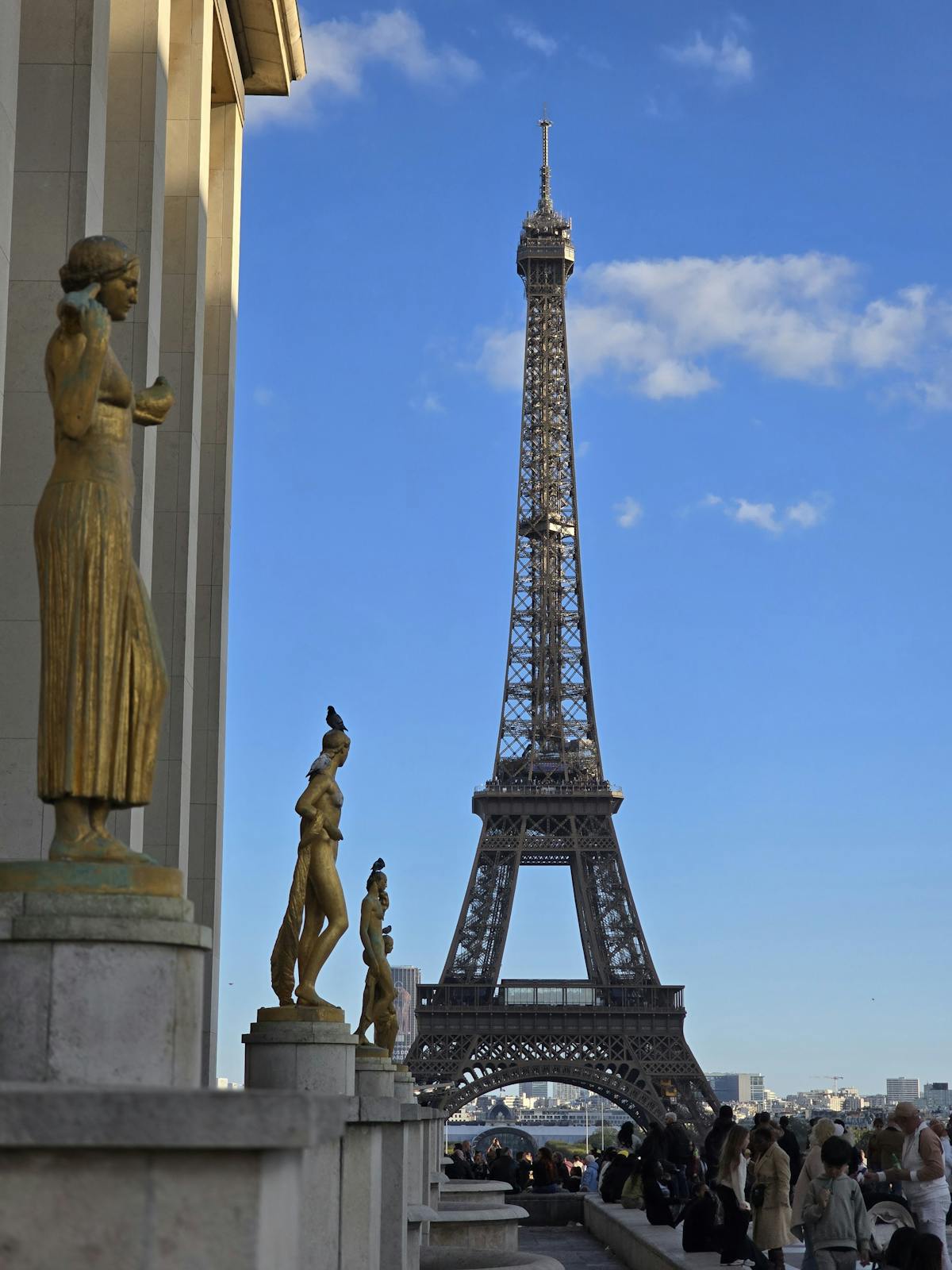The Eiffel Tower framed by golden Trocadero statues on a sunny afternoon