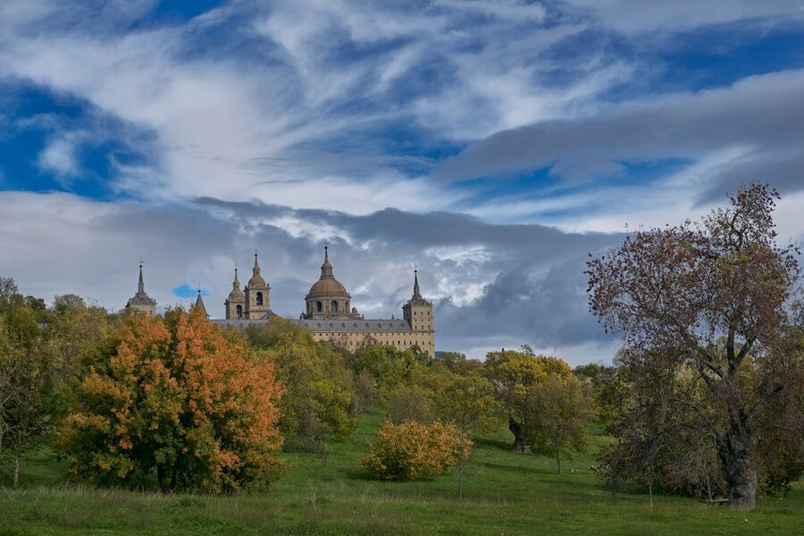 El Escorial monastery framed by autumn foliage under dramatic clouds