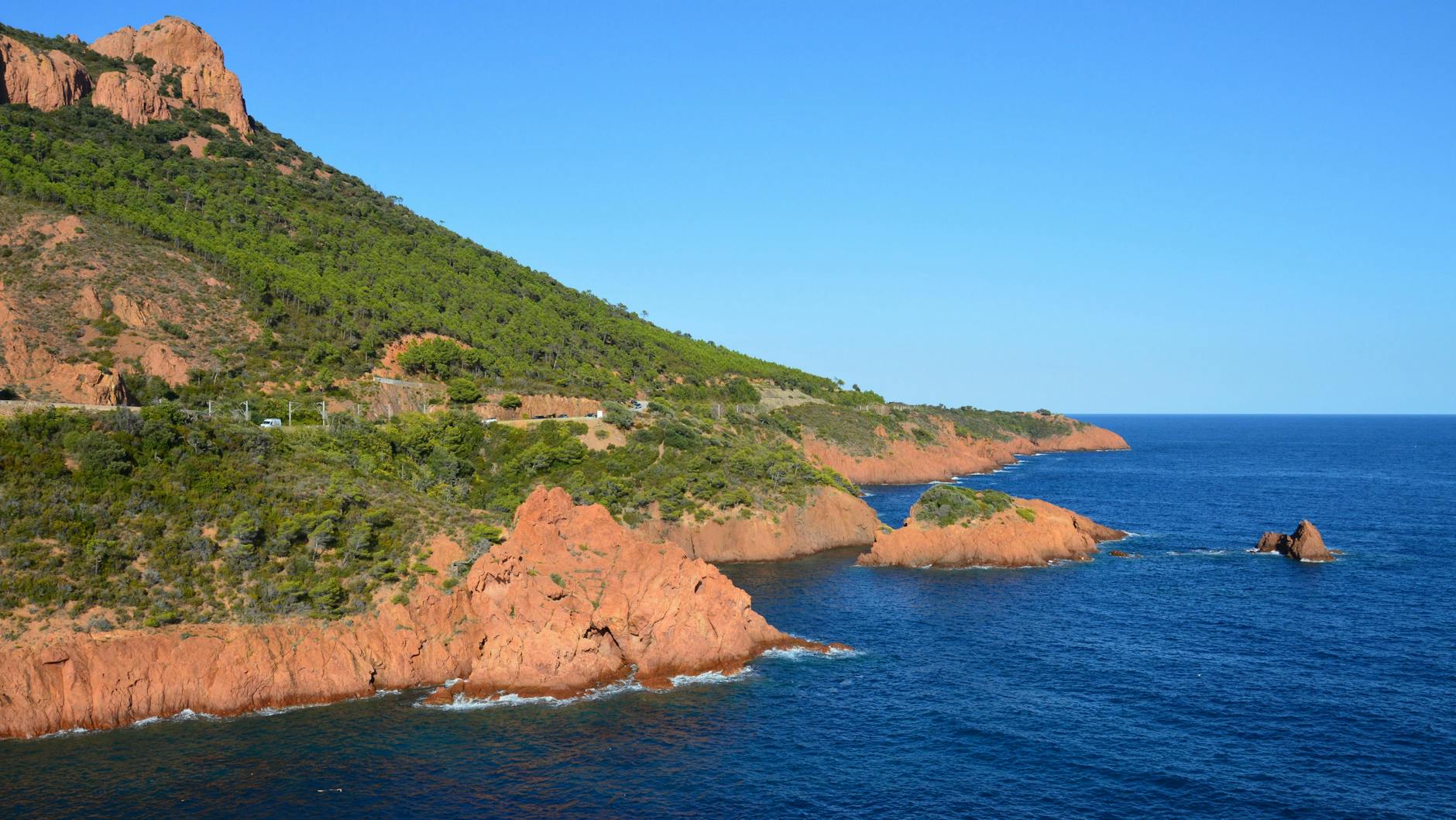 Rust-coloured rocky cliffs of the Esterel Massif rising from bright blue sea