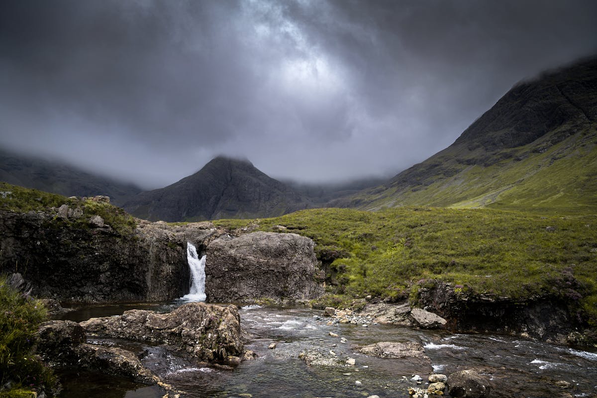 A waterfall cascading into a pool in the Isle of Skye with mountains in the background