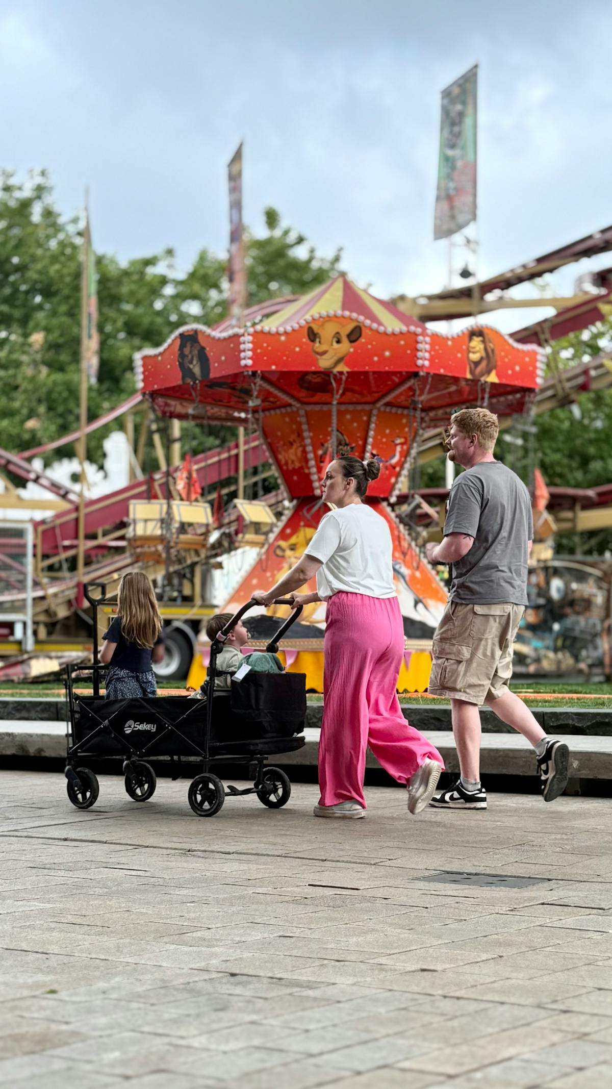 Family with stroller walking past colorful rides at an amusement park