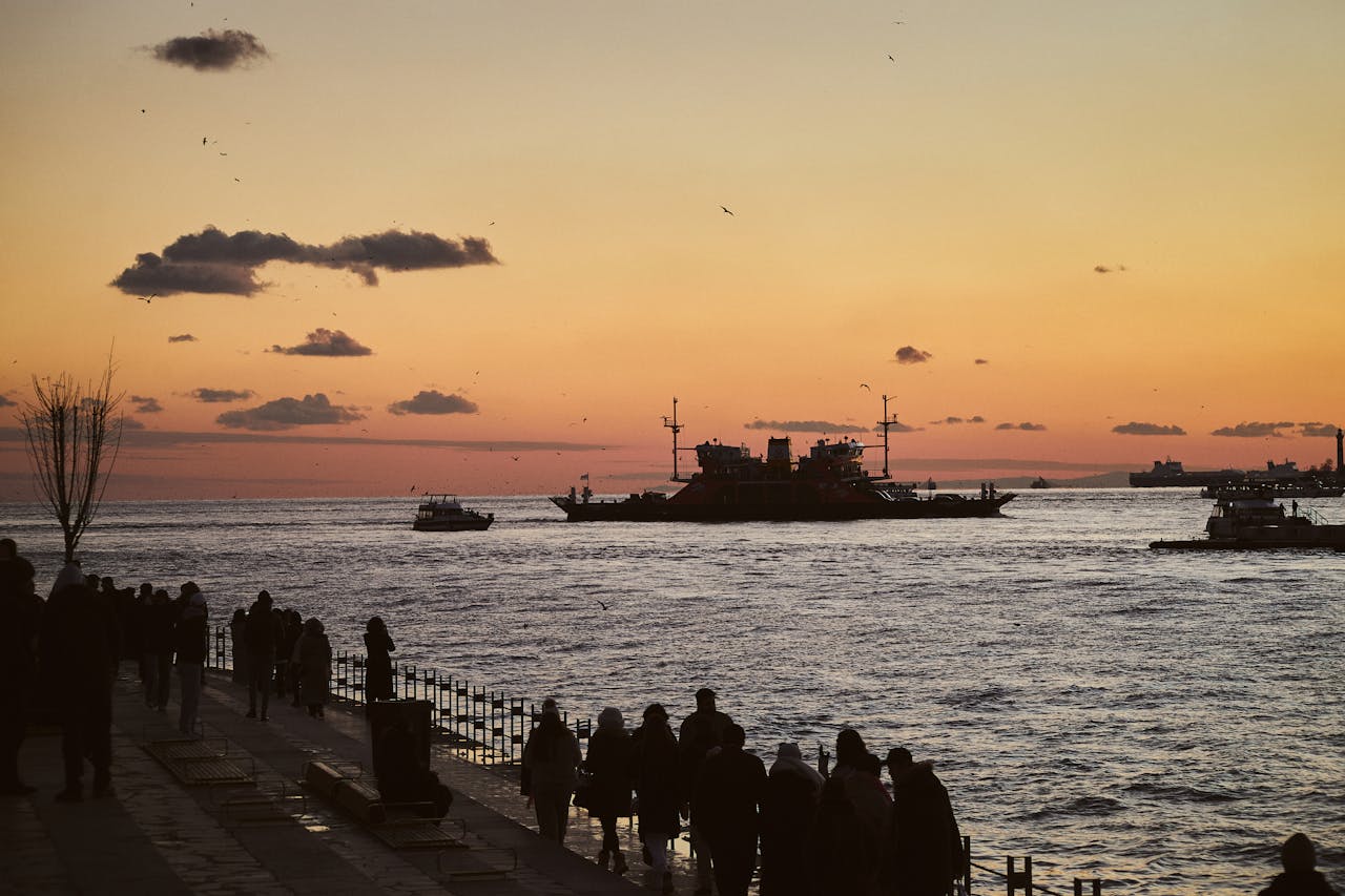 Ferries and boats on the Bosphorus at sunset with people walking along the waterfront in Istanbul