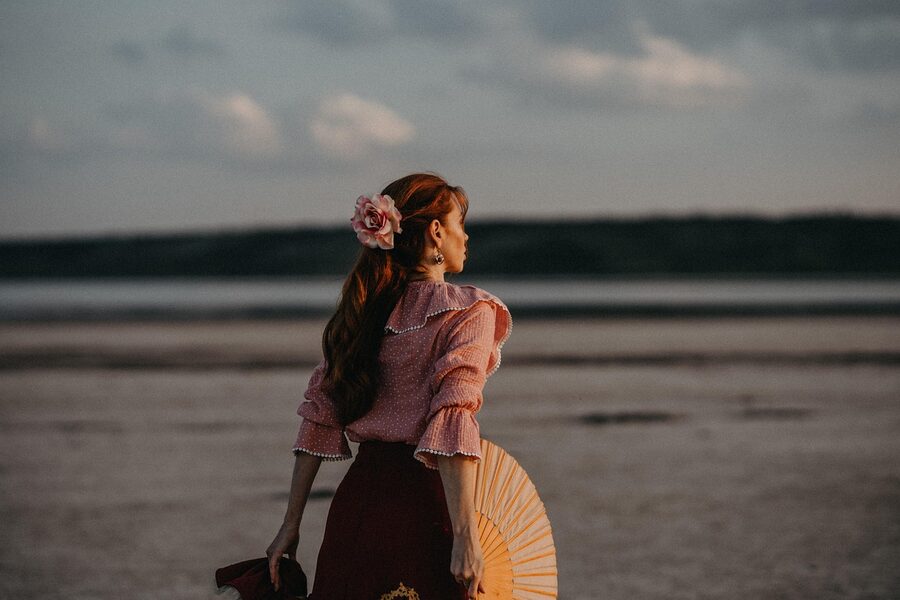 A woman dancing flamenco with a fan at sunset on a beach