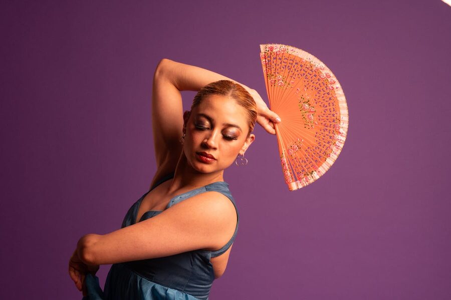 Woman in blue dress performing flamenco with a fan against a purple background