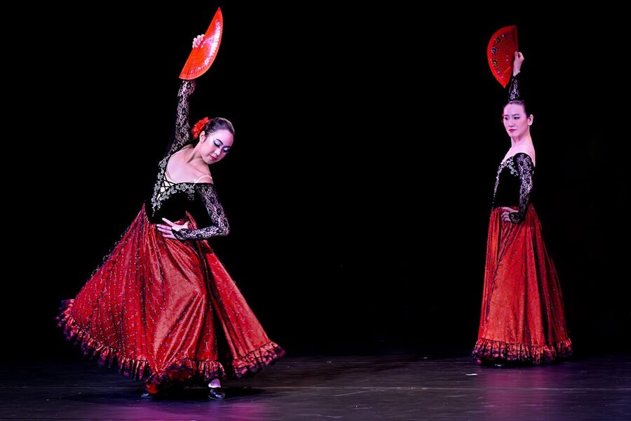 Two flamenco dancers performing with red fans in elegant show