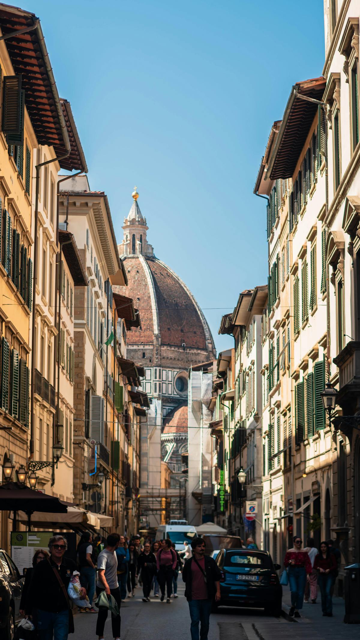 Charming Florence street view showing the Cathedral dome rising above historic buildings under blue sky