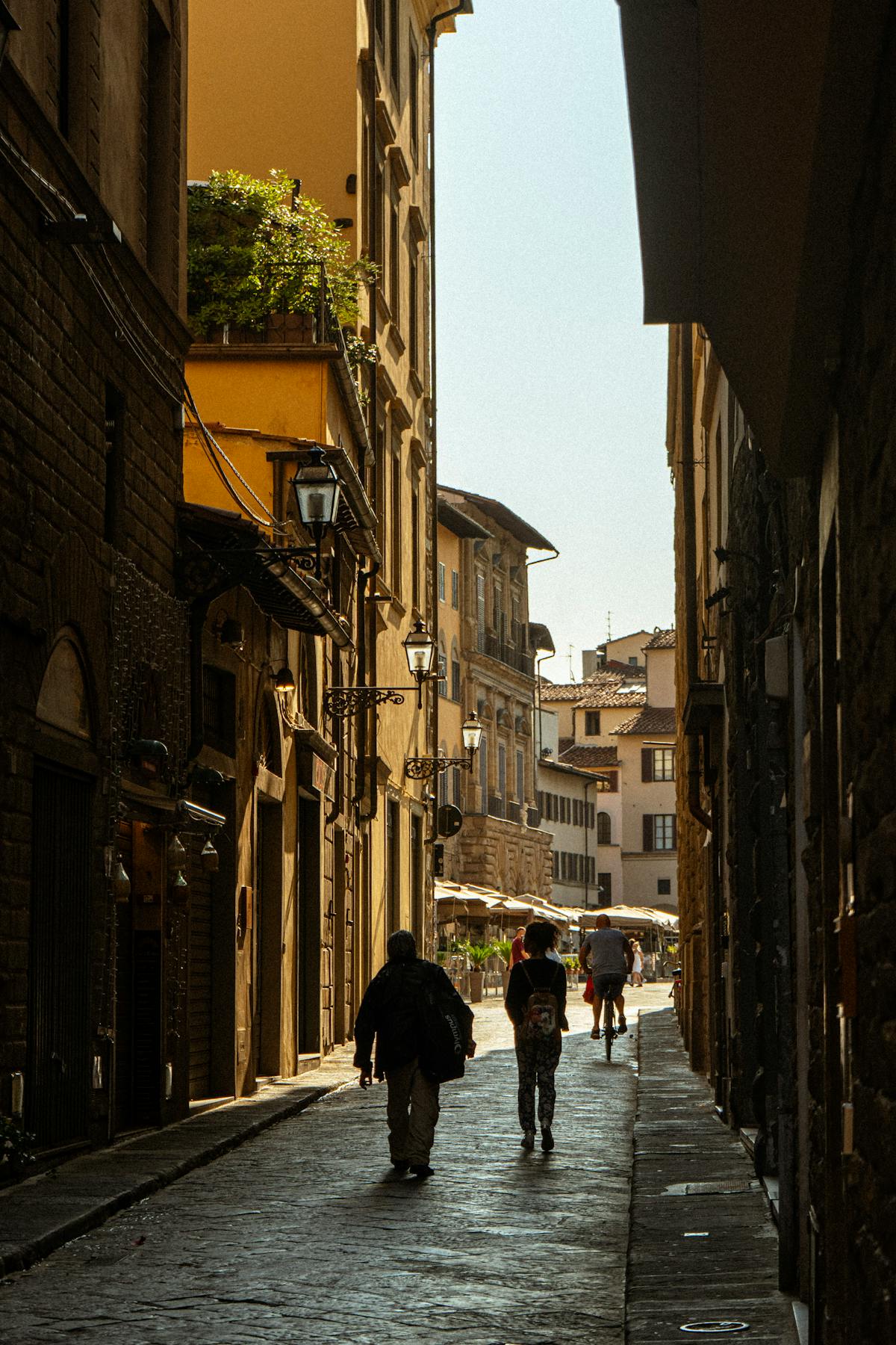 Silhouettes of pedestrians walking down a sunlit street in historic Florence