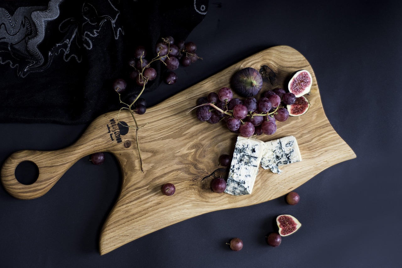 Artisan cheese board with grapes, figs, and wine on a wooden cutting board
