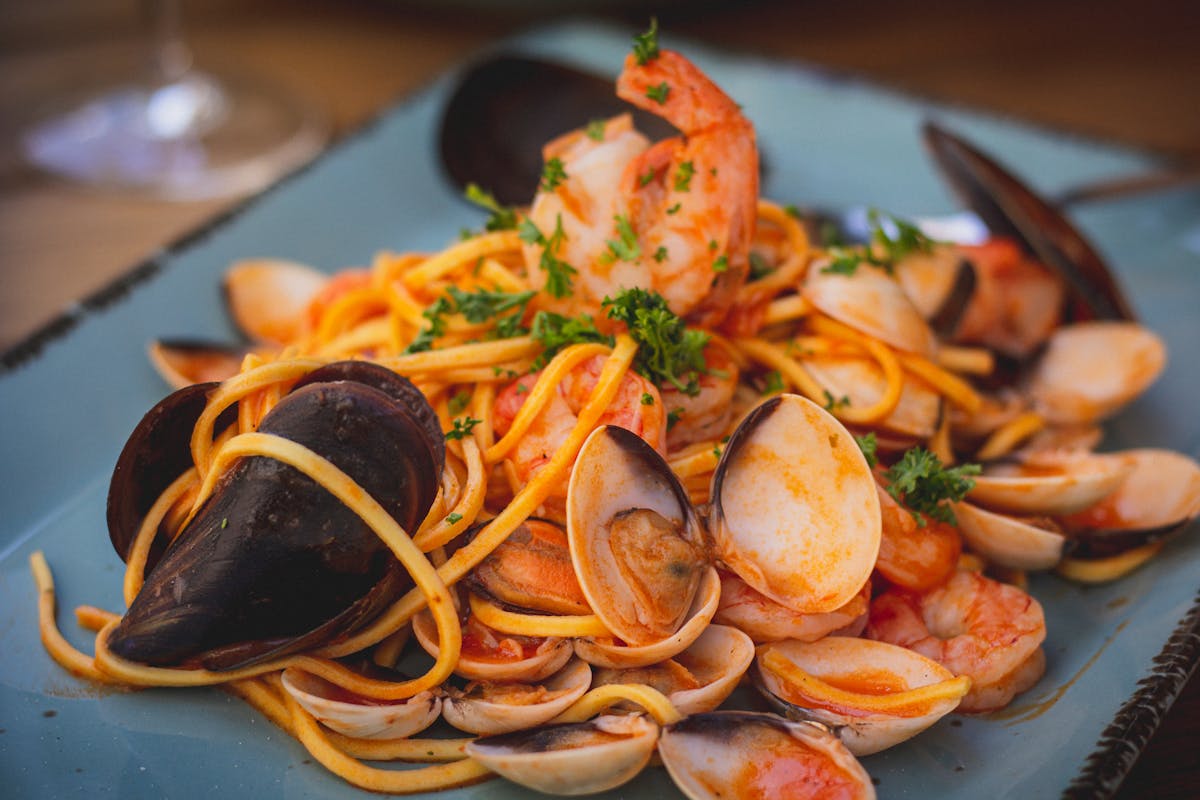Close-up of Mediterranean seafood pasta with mussels and prawns on a blue plate