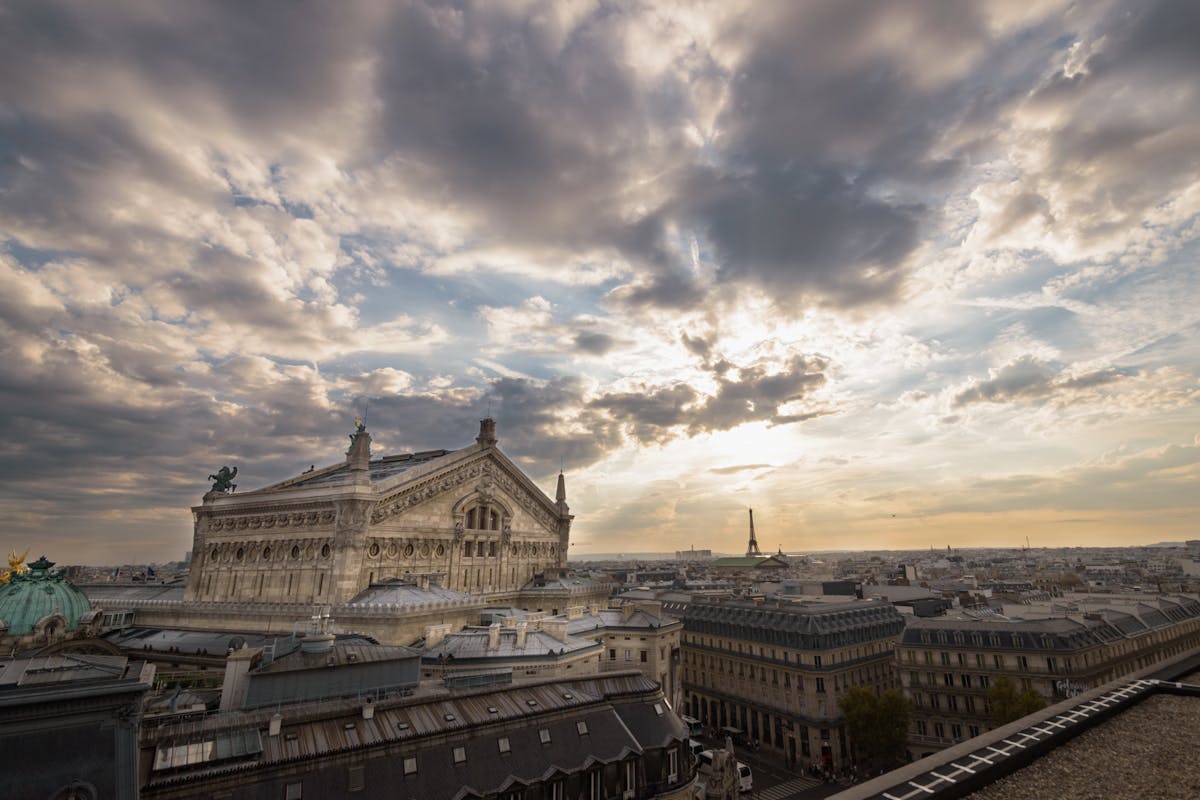View of the Palais Garnier in Paris under a dramatic sunset with the Eiffel Tower in the distance