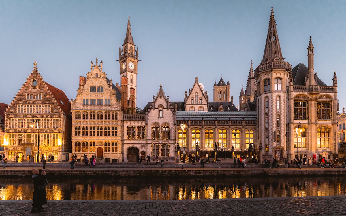 Medieval guild buildings illuminated at twilight along canal in Ghent Belgium