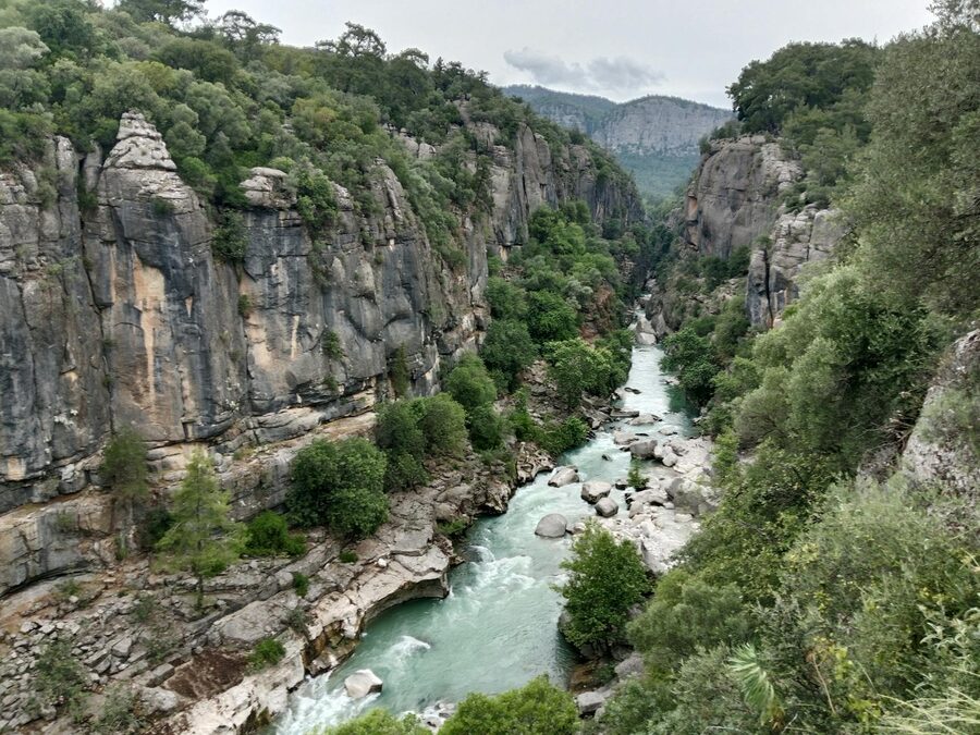 Deep gorge with turquoise river flowing between high rocky cliffs covered in greenery
