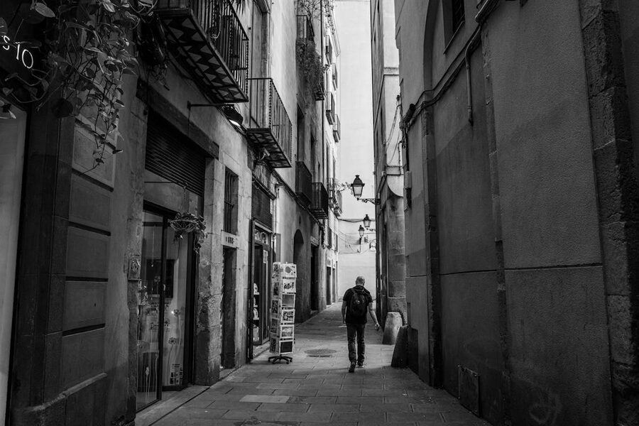 Black and white photo of a person walking through a narrow Gothic Quarter alley