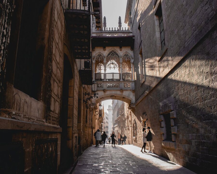 People walking under Pont del Bisbe bridge in Barcelona Gothic Quarter