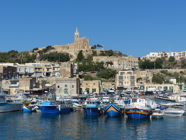 Boats at Mgarr harbour entrance with church in background Gozo