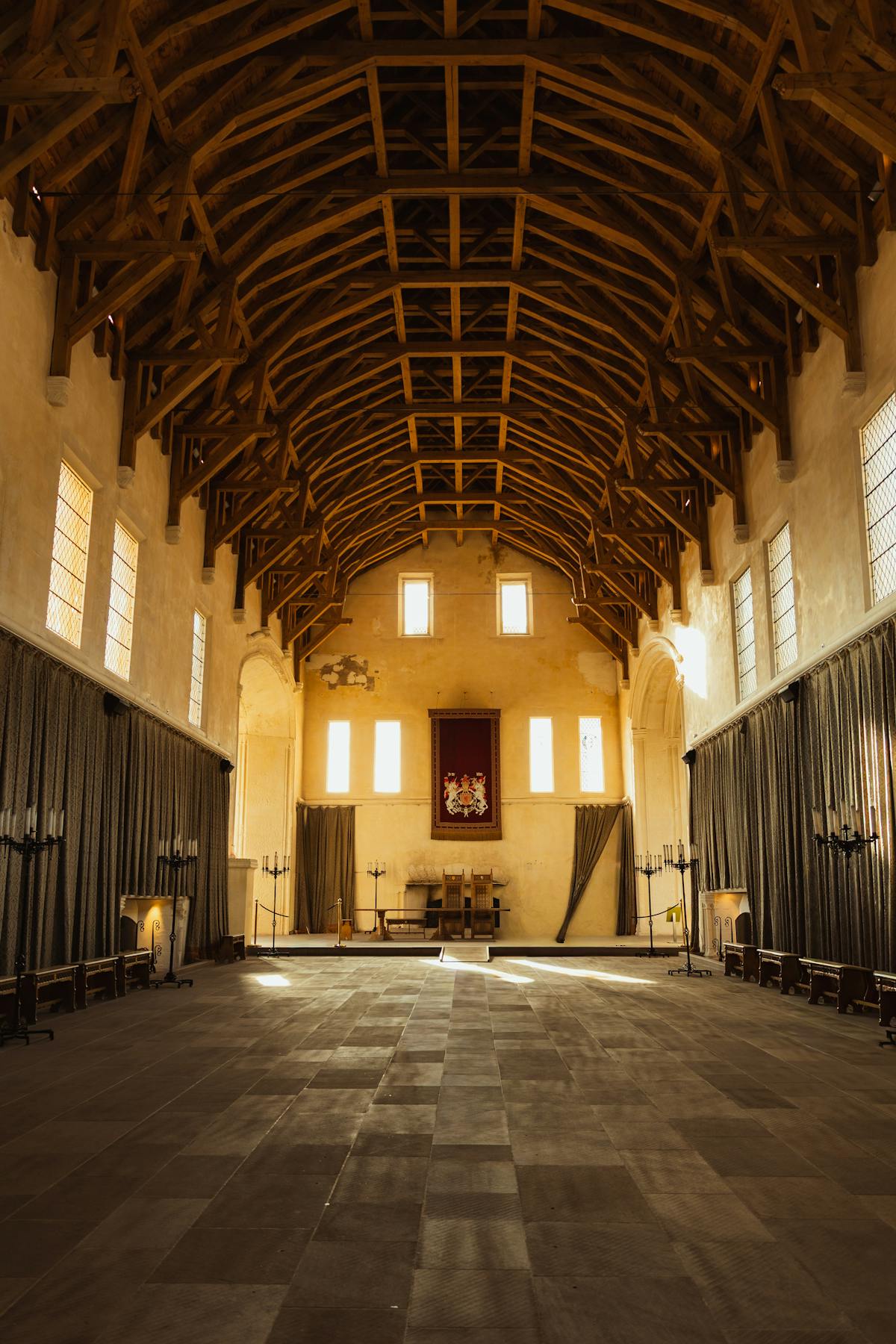 Interior of a grand medieval-style hall with wooden ceiling beams and natural light
