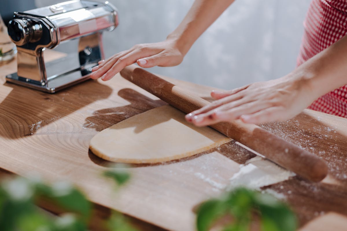 Close-up of hands rolling pasta dough on a wooden board during a cooking class
