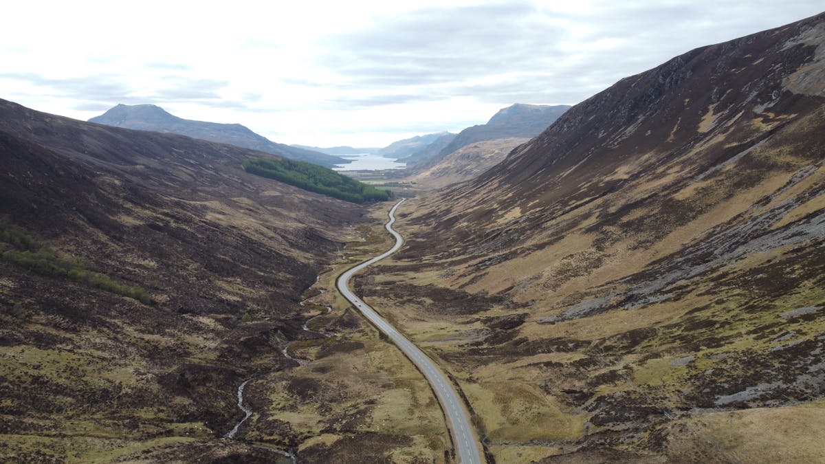 Aerial view of a winding road through a scenic valley in the Scottish Highlands