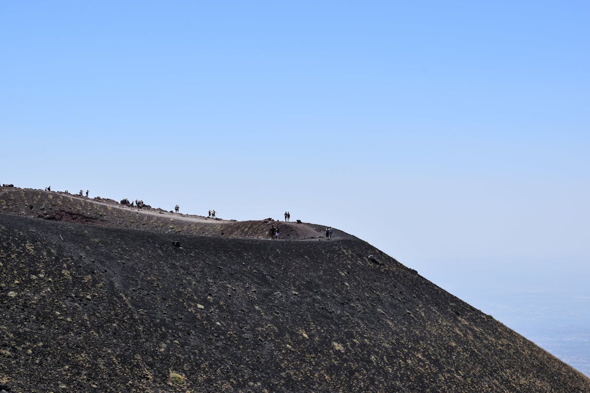 Group of hikers ascending Mount Etna against a clear blue sky