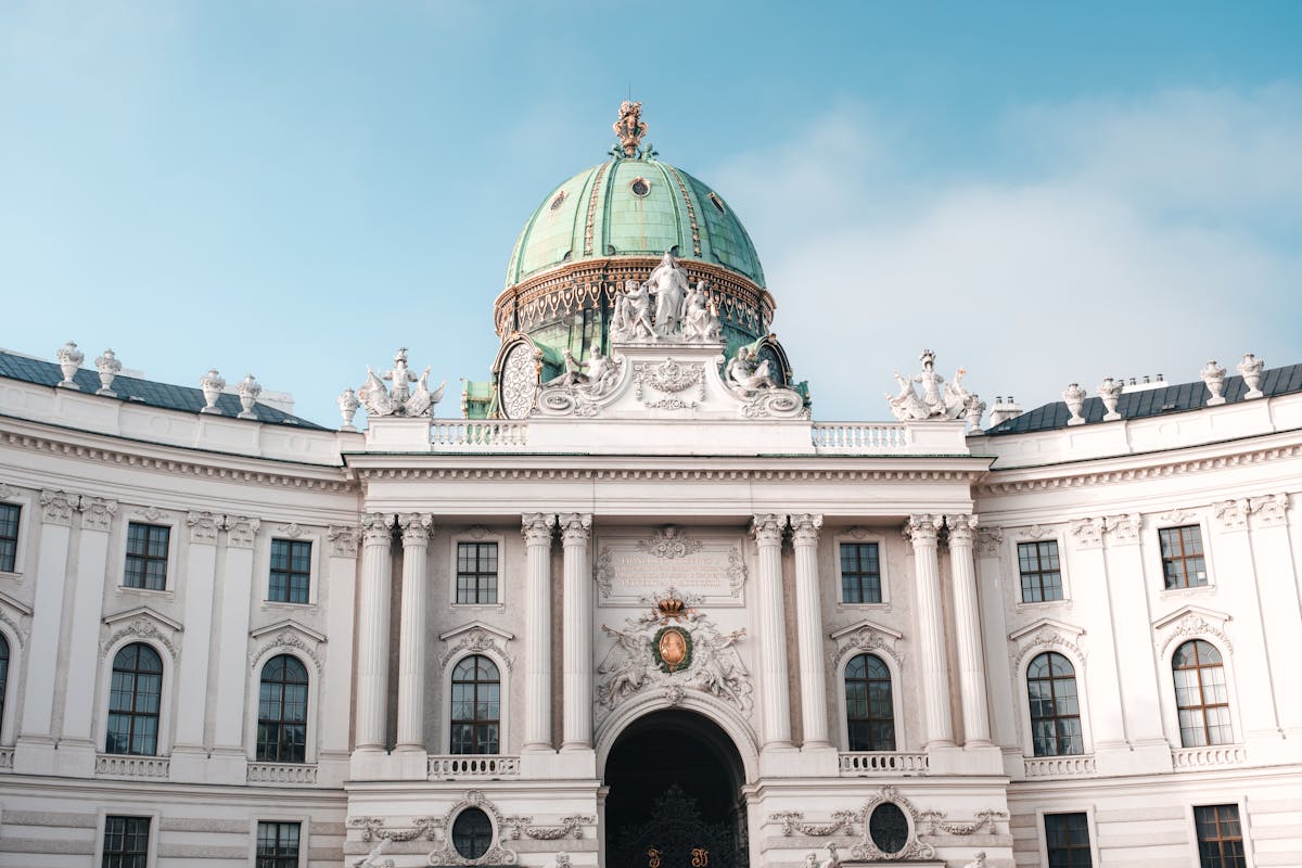 The ornate green dome and baroque facade of the Hofburg Palace in Vienna against a clear sky