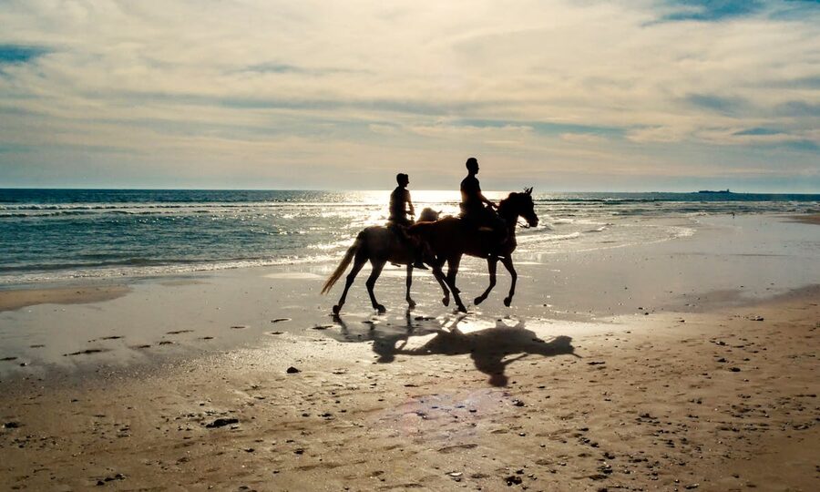 Two people horse riding along the beach at sunset in southern Spain
