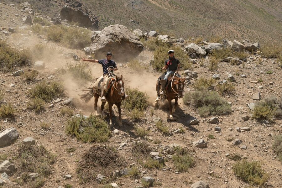 Two horseback riders navigating rocky dusty desert terrain