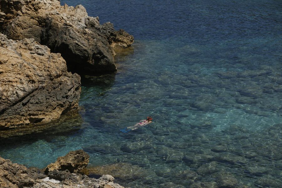 Woman snorkeling near rocky shore in Ibiza clear waters on a summer day