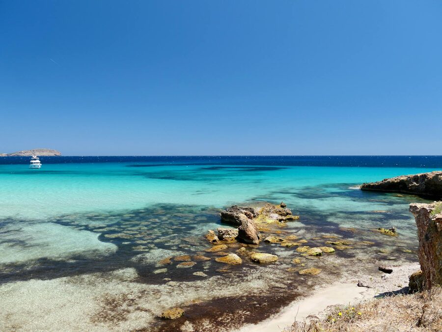 Turquoise waters and rocky coastline of Ibiza beach under clear blue sky