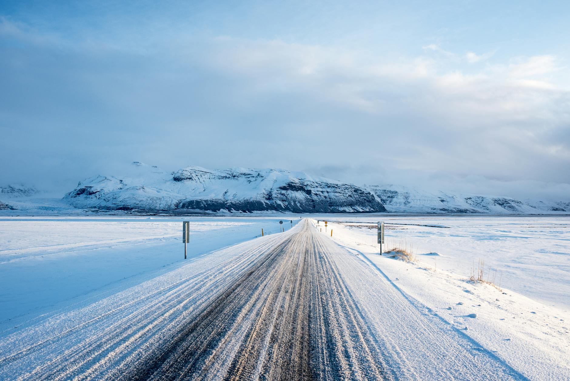Snow covered road leading to mountains in Iceland with clear blue sky