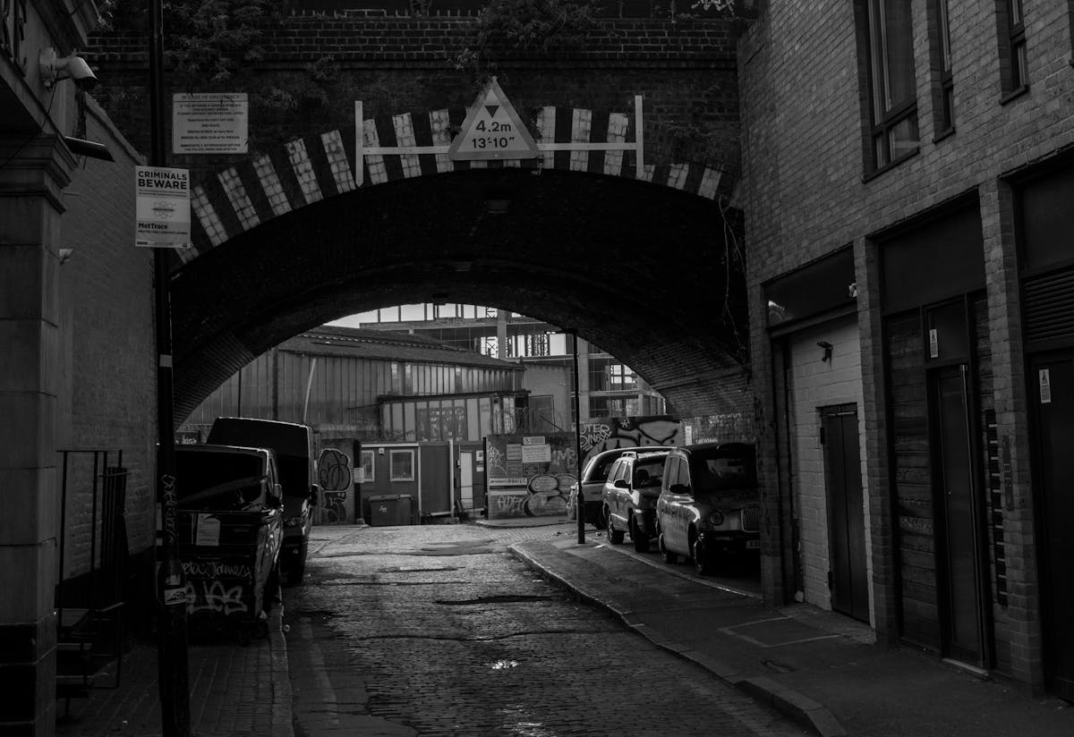 A moody black and white view of a London street passing under a stone arch