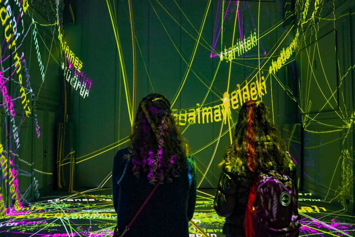 Two women observing a dynamic text projection art installation in a dark room