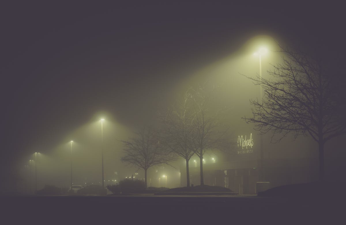 A foggy street at night illuminated by glowing lamp posts and bare winter trees