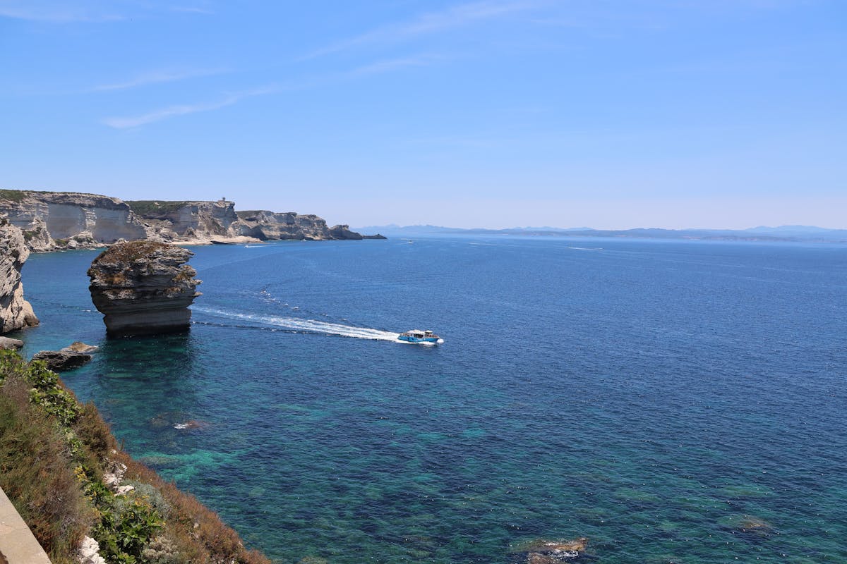 Boat near Bonifacio sea caves with turquoise water and white limestone cliffs