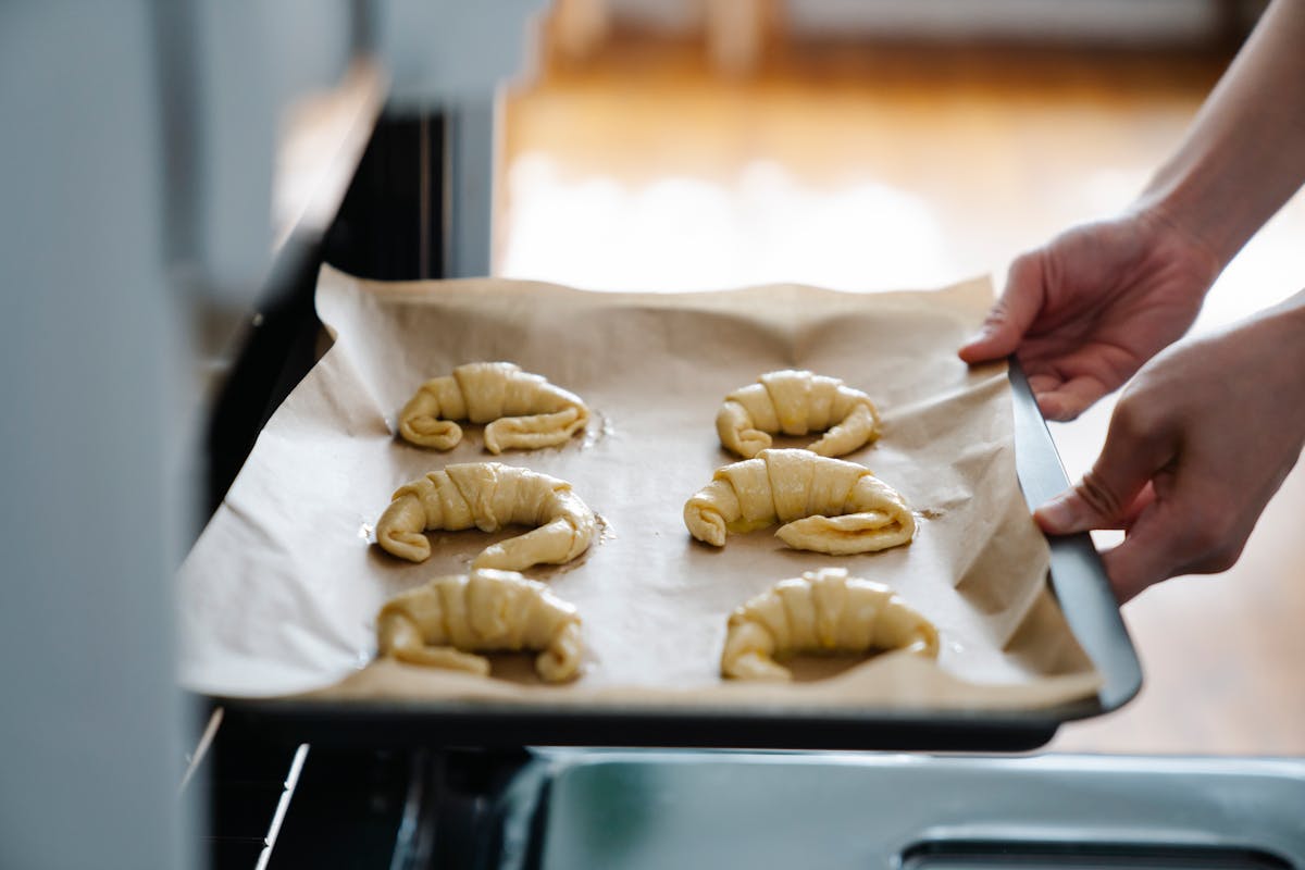 Hands placing homemade croissants on a baking tray before baking