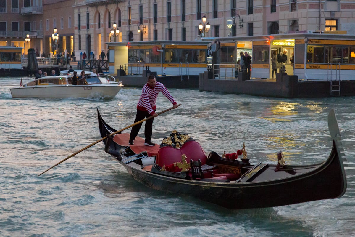 Gondolier navigates a gondola on a Venetian canal at dusk