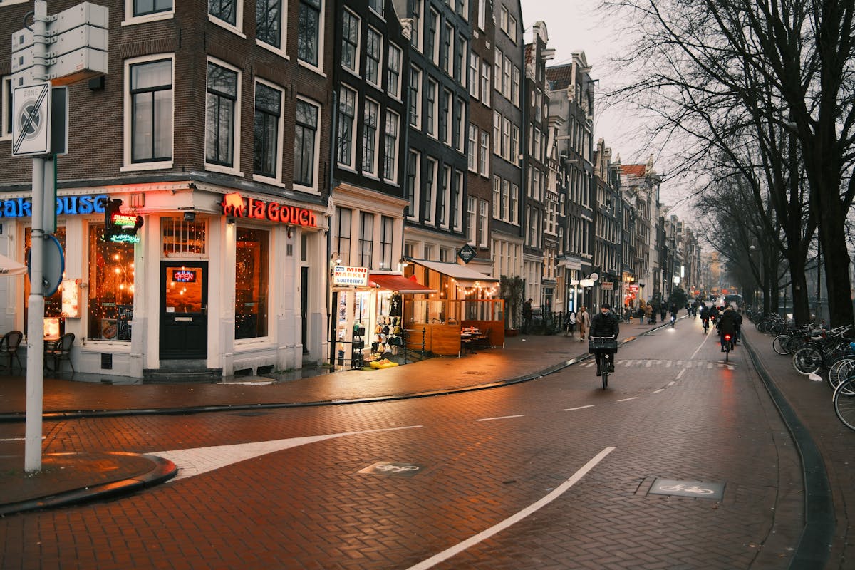 Quaint Amsterdam street view at dusk with bicyclists passing by iconic Dutch architecture
