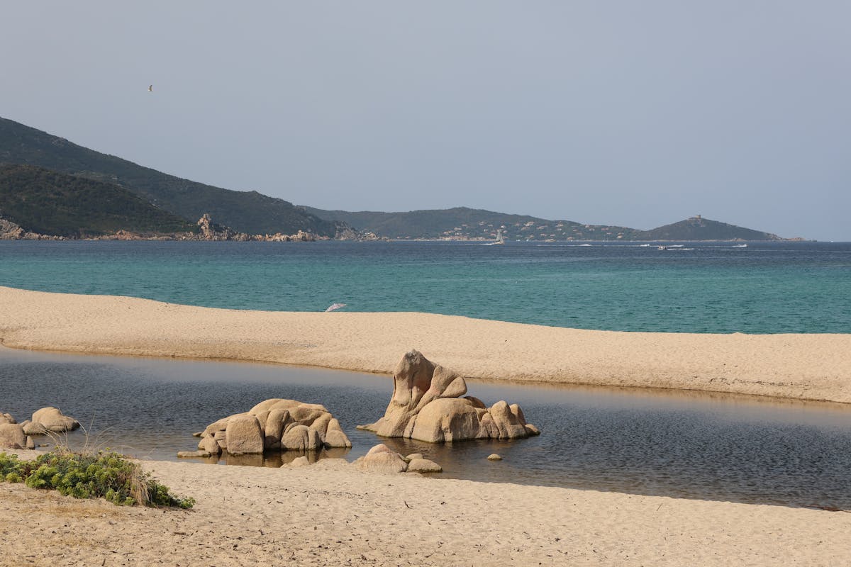 Sandy beach with clear turquoise water and rocky shoreline in Corsica