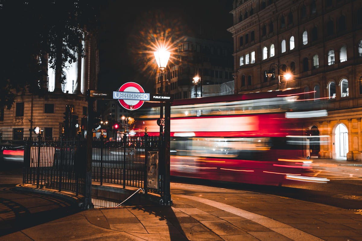 Night scene of a red double-decker bus passing by a London Underground entrance