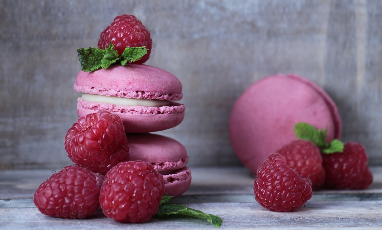 Pink raspberry macarons with fresh raspberries on a plate