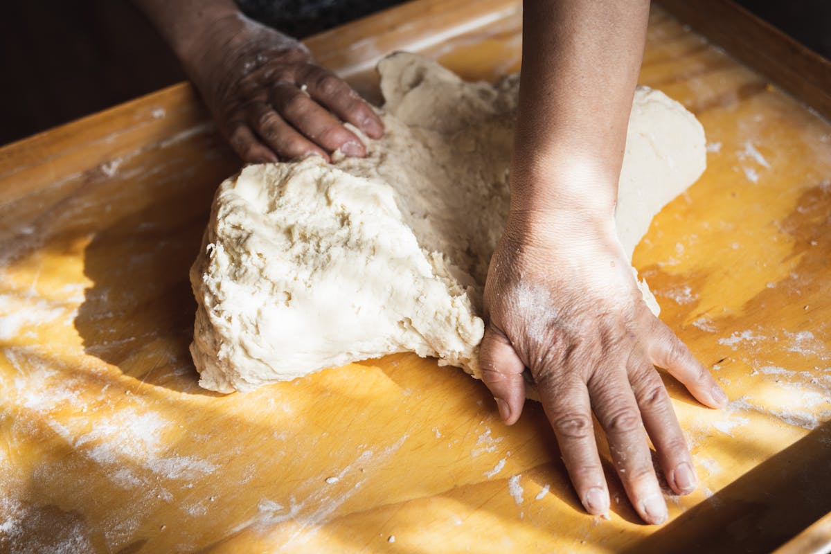Person kneading bread dough on a floured wooden surface