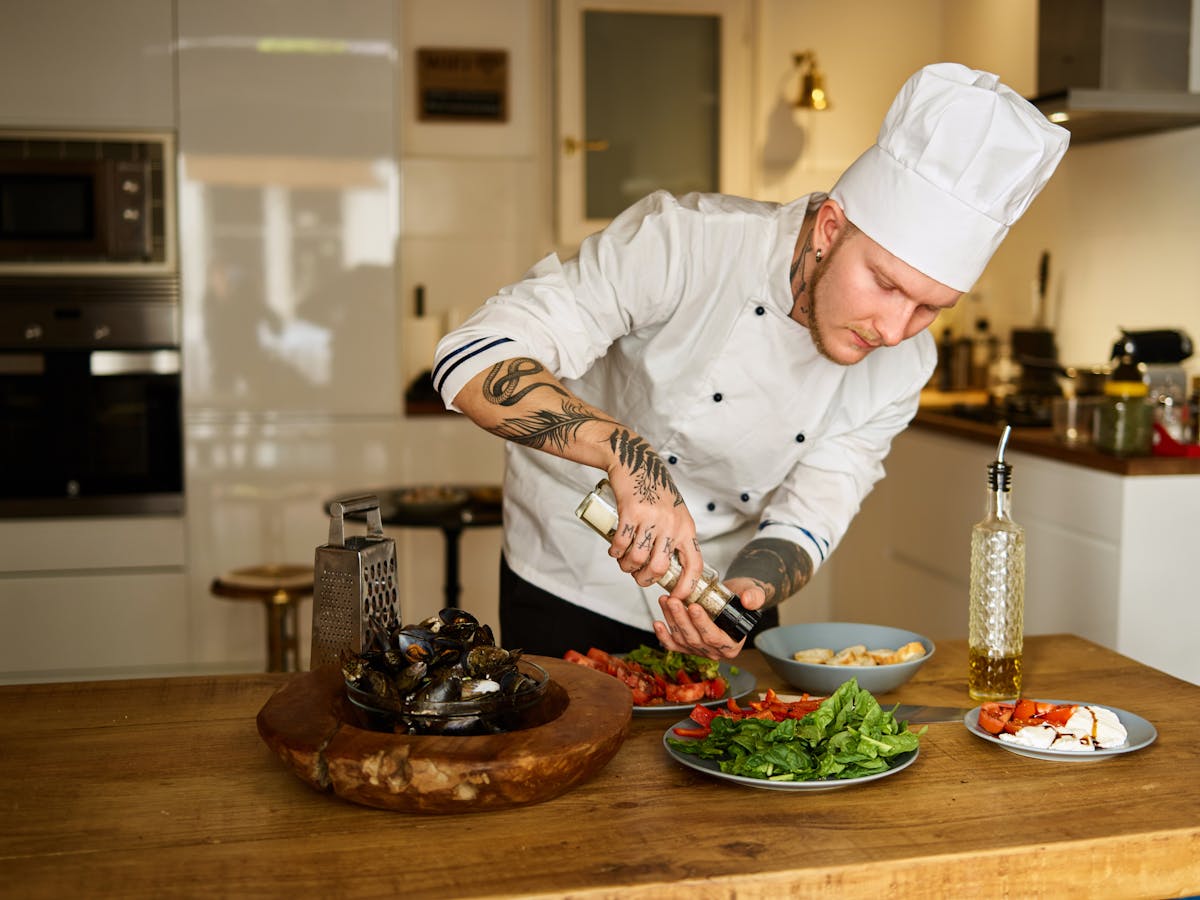 Chef in white uniform seasoning fresh vegetables in a professional kitchen
