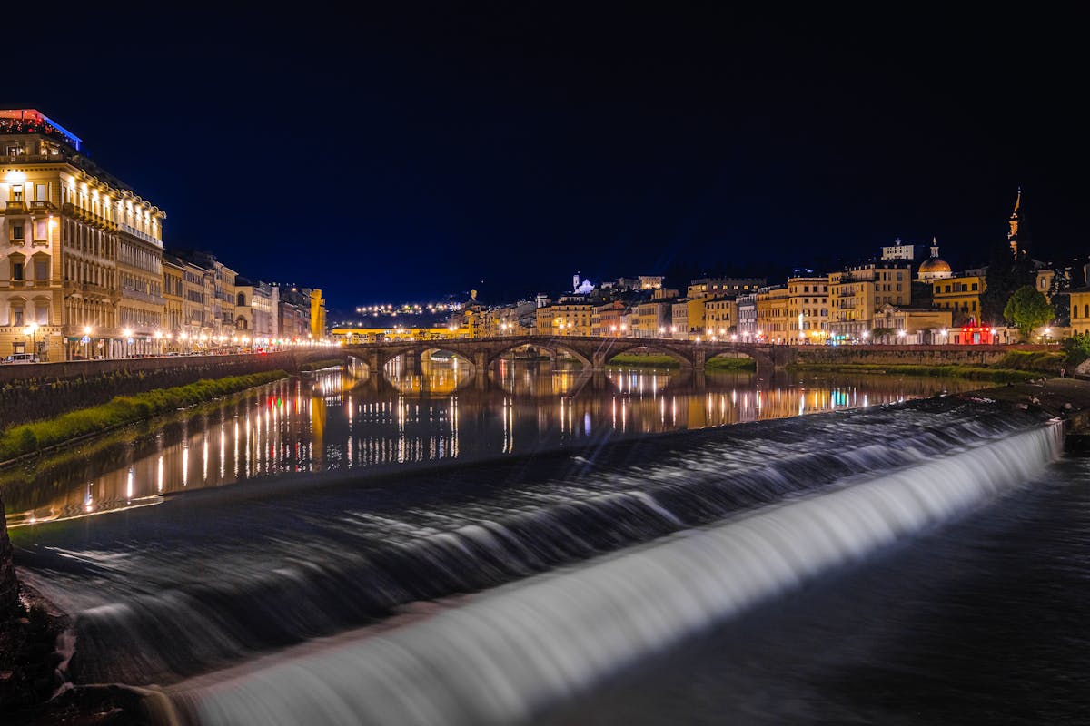 Beautiful nighttime scenery of Florence Arno River with illuminated buildings and bridge reflections