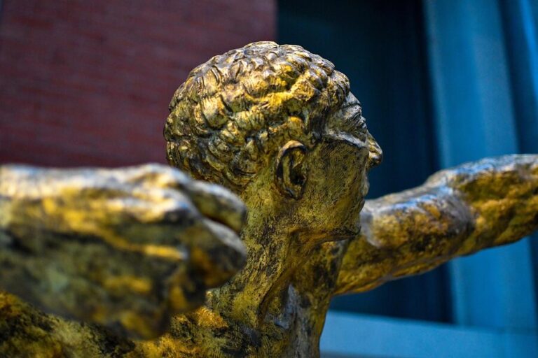 Ancient bronze statue displayed in a museum gallery with Greek archaeological artifacts