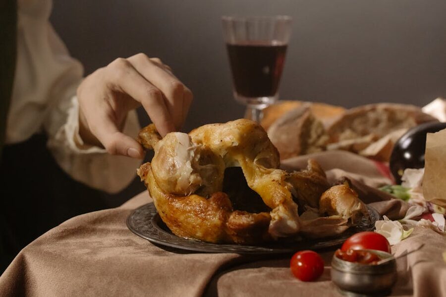 A hand reaches for roast chicken on a renaissance-style table