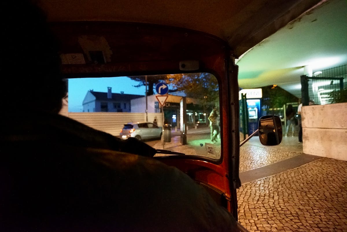 View from inside a tuk-tuk driving through a Lisbon street with the driver visible in front