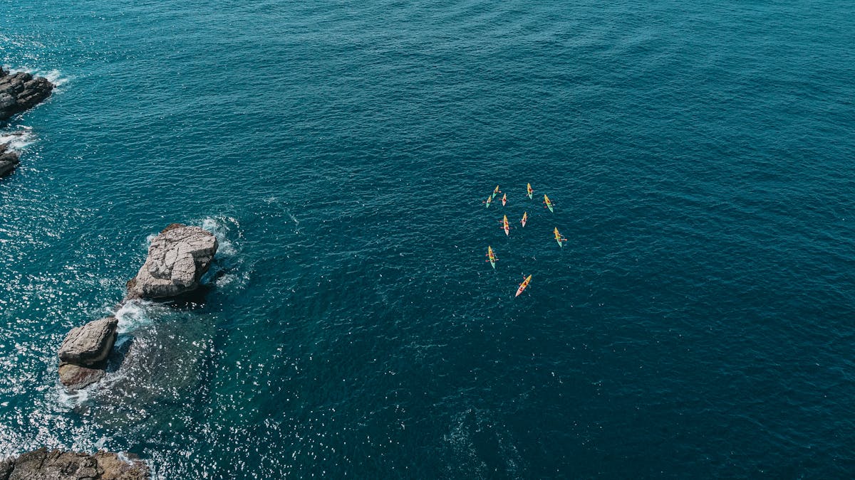 Aerial shot of kayakers navigating blue waters near a rocky coastline under clear skies