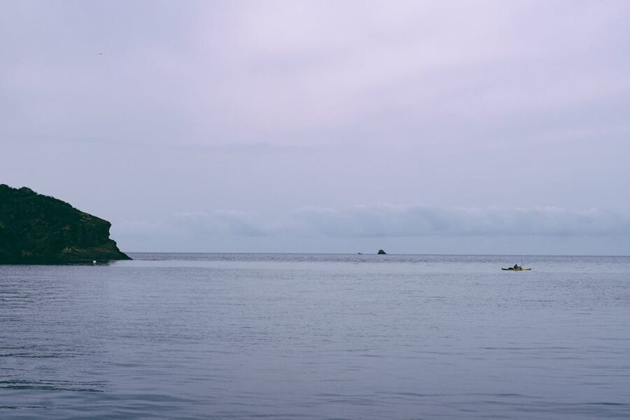A lone kayaker on calm waters beside a tall rugged cliff face