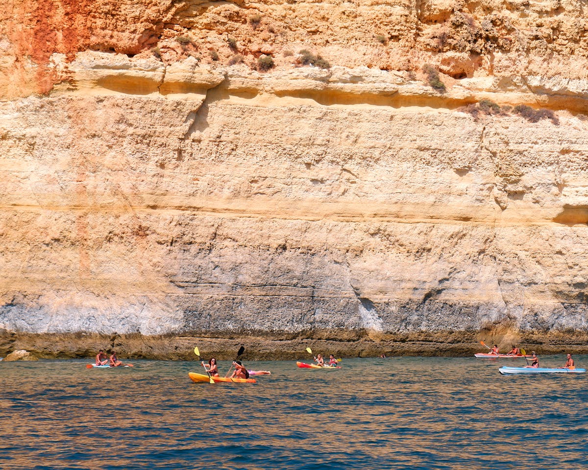 Person kayaking along tall golden Algarve cliffs with clear turquoise water