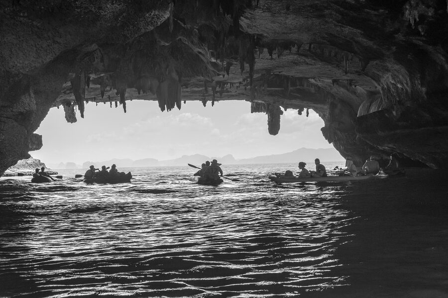Kayaker silhouetted inside a dark sea cave with light streaming in from the entrance