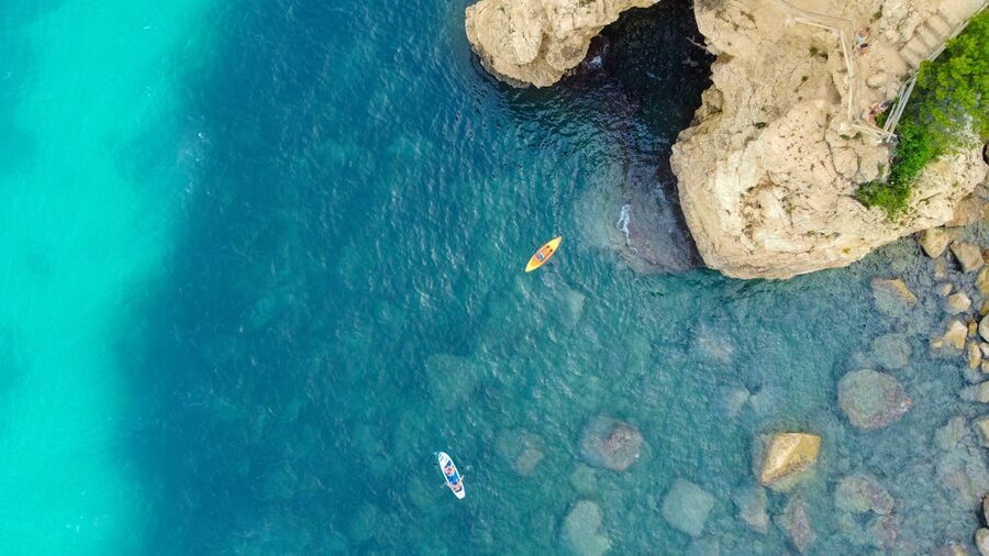 Aerial view of kayaks paddling near dramatic rocky cliffs along the Spanish coastline
